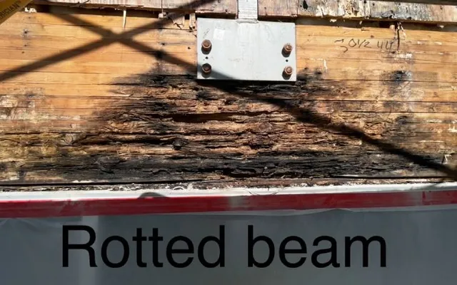 Rotted structural beam uncovered behind the failed facade — moisture damage found during inspection
