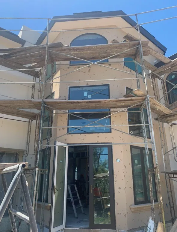 Brown coat stucco on the arched entry tower with scaffolding and reclaimed timber staging (during)