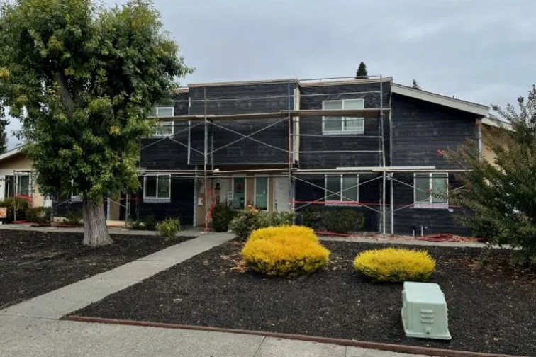 Building wrapped in weather-resistive barrier with scaffolding during a re-stucco (during) — moisture barrier installation